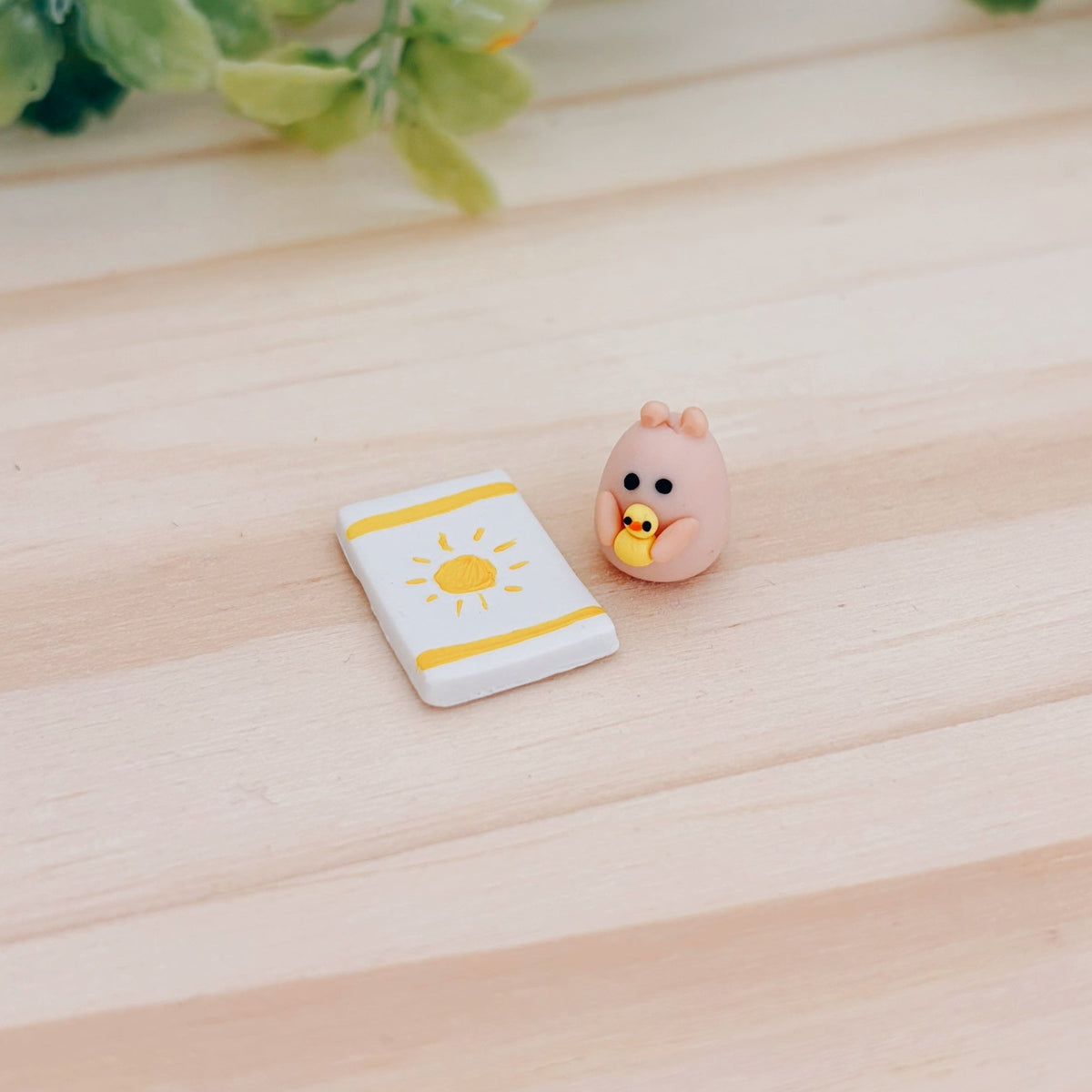 Miniature hamster clay figurine holding a duck next to a clay beach towel with a sun and stripes pattern