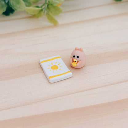 Miniature hamster clay figurine holding a duck next to a clay beach towel with a sun and stripes pattern